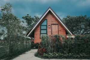 Cozy wooden A-frame tiny house surrounded by lush greenery and vibrant plants outdoors.